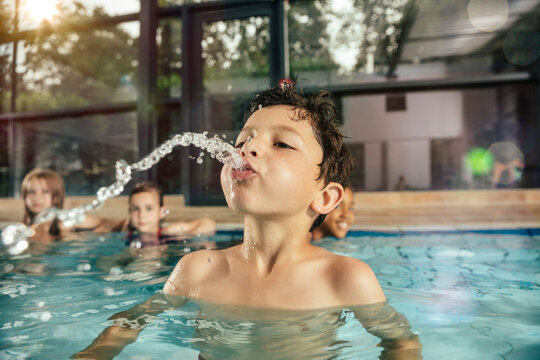 Boy with friends in indoor swimming pool spitting water