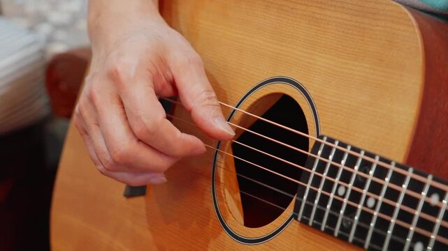 Close-up of fingers gently strumming acoustic guitar strings