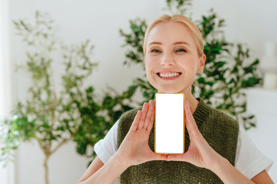 Happy woman shows blank smartphone screen indoors