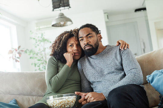 Couple shocked watching horror movie sitting at sofa at home