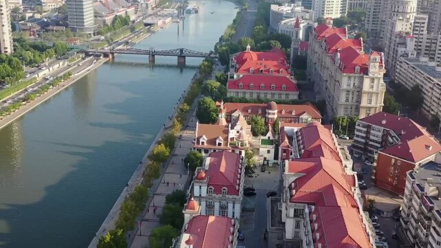 Aerial drone footage of historic European-style buildings with red-tiled roofs lining the Hai River in Tianjin, featuring a steel truss bridge and modern city skyline in the background