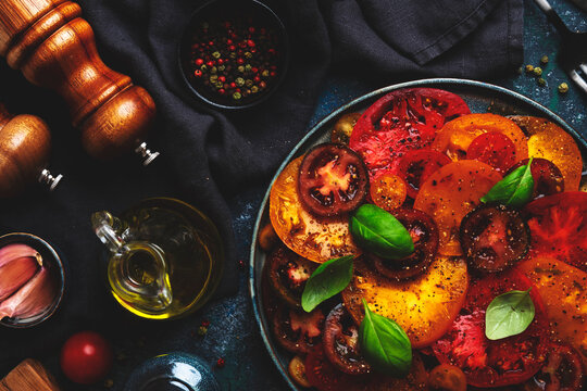 Gourmet fresh tomato salad with basil near pepper grinder. Clean eating dietary holistic health trend. Raw organic vegetables diet dinner meal preparation concept on dark tabletop.