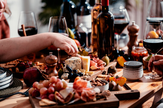 Red wine glass in hand during family autumn lunch - friends sharing gourmet charcuterie platter in cozy restaurant setting. Festive celebration and fine dining tasting experience.