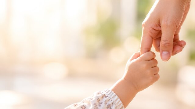 Small child holding a mother's finger against a soft neutral background, expressing family unity, emotional reassurance, tenderness, belonging, hope, unconditional love and lifelong connection.