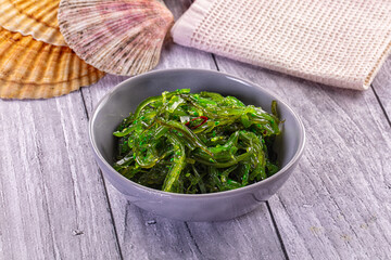 Vibrant green wakame seaweed salad served in gray ceramic bowl on rustic wooden table with seashell decorations © Andrei Starostin