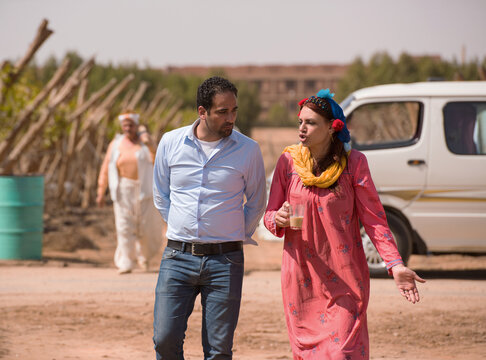 Middle Eastern couple engaged in animated candid conversation while walking together on rural farm pathway woman in colorful traditional embroidered