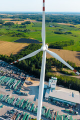 Aerial view of a wind turbine standing above rows of solar panels in a vibrant green field © AlexGo