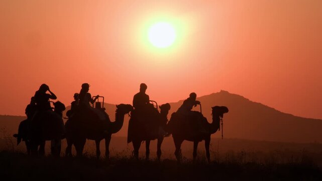 Silhouettes of people riding camels watching sunset during tourist excursion in mountain valley Cappadocia