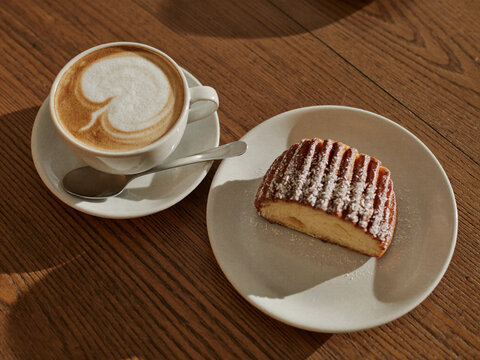 Cappuccino with latte art and coconut topped cake slice on wooden table in warm sunlight, top view cafe scene