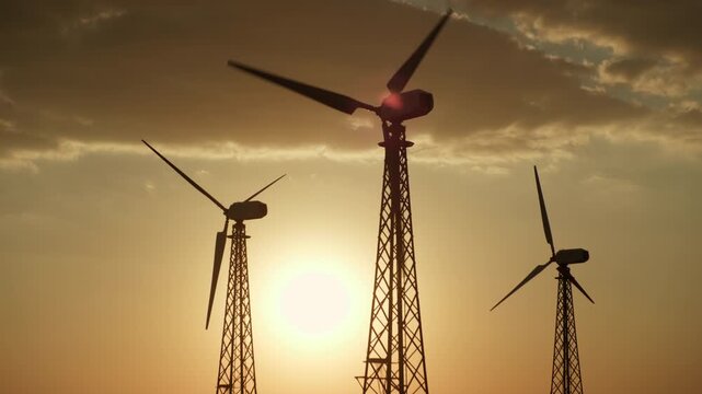 Silhouettes of wind turbines generator power plant against background of sunset sky with sun
