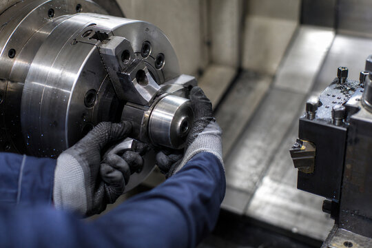 Industrial worker wearing protective gloves installing a metal component in a CNC lathe chuck. Precision machining, manufacturing technology and engineering production process.