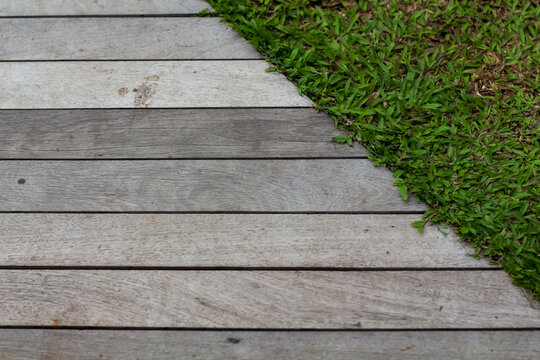 Weathered wooden deck boards meet a patch of green grass in a simple outdoor ground-level view