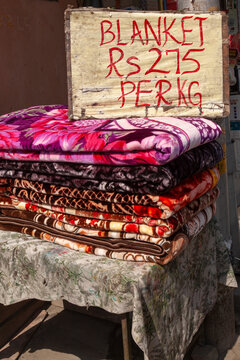 Stack of colourful blankets for sale with a handwritten price sign, Jammu and Kashmir, Srinagar, India