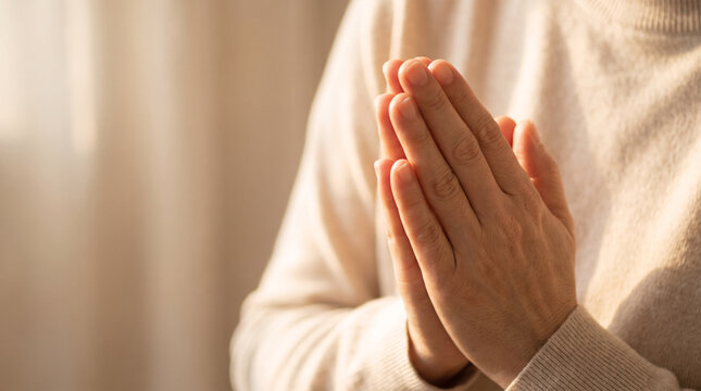 Hands pressed together in namaste before the chest of a person in a cream knit sweater