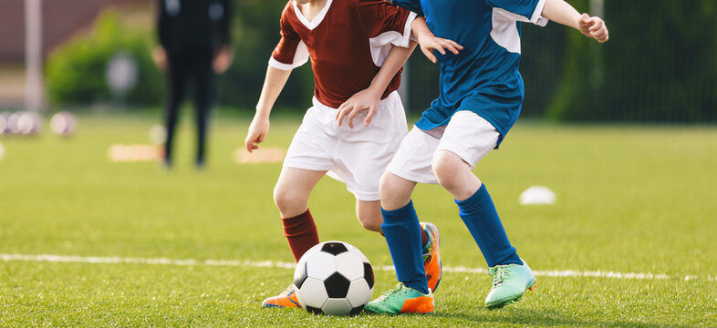 Kids in Football Game. Junior Soccer Players in Red and Blue Kits Battling for Ball Possession During Youth Football Match on Grass Pitch