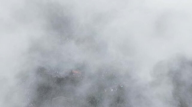 Aerial view of Thann town partially obscured by thick clouds with visible rooftops and streets in Thann, Grand Est, France.