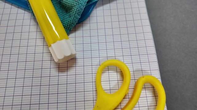 A close view of classroom materials on squared exercise books includes a small globe, colored pencils, yellow glue stick, white eraser, scissors and turquoise cloth.