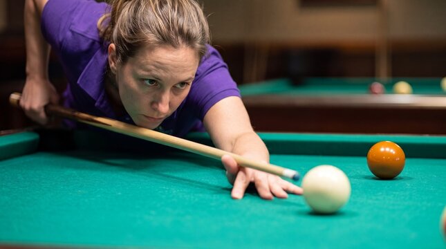 focused young woman leaning over table aiming cue stick at billiard ball
