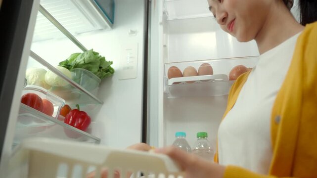 Woman placing fresh fruits and vegetables into a refrigerator to maintain freshness, highlighting healthy eating, food preservation, proper storage and an organized kitchen.
