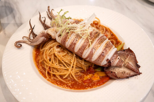 Grilled whole squid spaghetti pasta with tomato sauce on white plate.