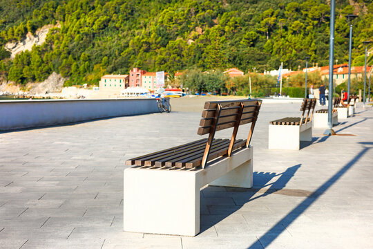 Empty wooden bench sunny seaside promenade. Vacation relaxation wellness calm mood. Travel destination urban living hospitality guide.