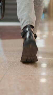 Someone lower leg and foot in black boots walking across different surfaces like polished tile floors and entering escalator. sequence shows transition from ground level movement