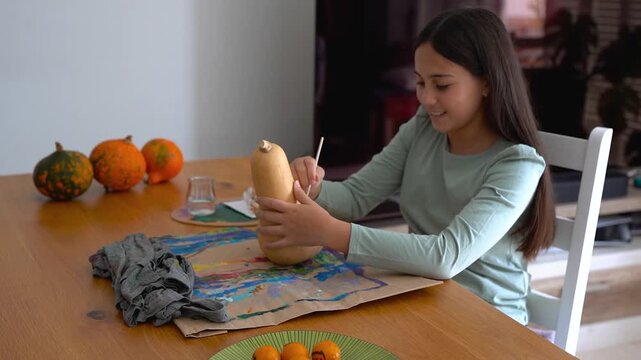 Young female kid painting on a pumpking during fall season for Halloween event - Holiday, childhood and autumn lifestyle concept	