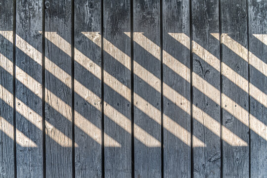Old weathered gray wooden planks with diagonal stripes of sunlight and shadow. Abstract geometric texture background.
