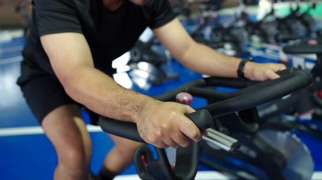 Close-up man exercising on a stationary bike at an indoor fitness center, improving cardiovascular health, building muscle endurance and supporting healthy aging and longevity.