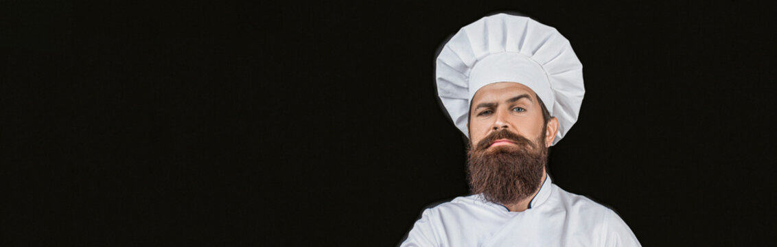 Confident bearded male chef in white uniform. Chef in uniform isolated on black background, copy space on side