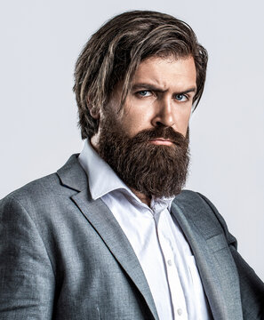 Closeup portrait of handsome businessman in formalwear suit. Portrait of confident businessman man, suit with beard and hair alone looking seriously and confidently at the camera on gray background