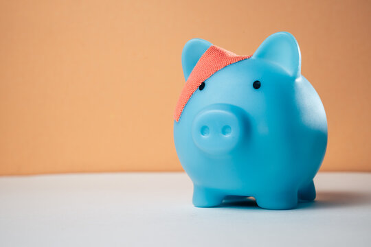 Piggy bank wrapped in a bandage on a plain background with copy space, representing financial recovery, debt relief, deposit protection, bankruptcy, business rehabilitation and a fresh start.