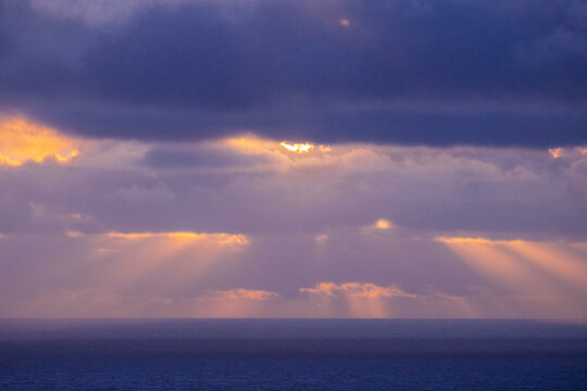 Sunlight piercing clouds over ocean horizon at sunrise in California
