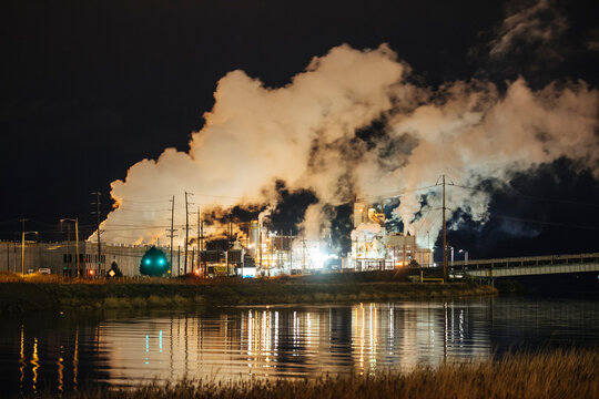 Industrial plant emitting smoke with water reflection at night