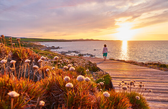 Italy, Sardinia, Lu Litarroni, senior woman on wooden boardwalk at sunset