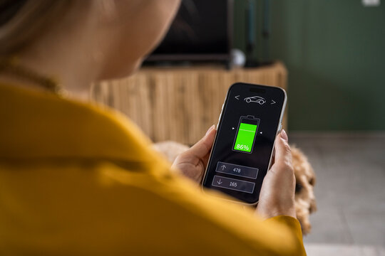 Woman checking electric car battery status on smartphone app at home