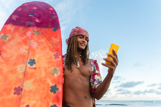 A male surfer checks his smartphone on a tropical beach