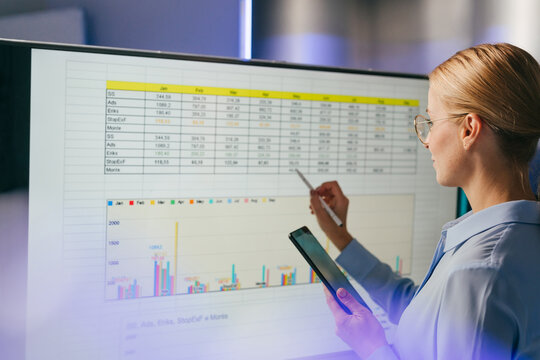 Businesswoman analyzing data on a large screen with a tablet indoors