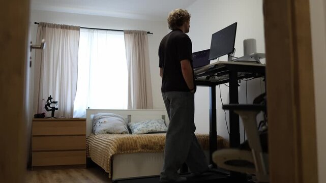 Young professional walks on an under desk treadmill while working at a standing desk with dual screens combining remote work and daily exercise in a modern home office setting