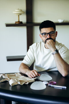 Male plastic surgeon sitting at a desk with breast implants and medical instruments, consulting on aesthetic surgery