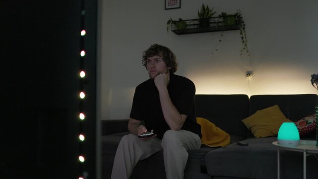 Young man switches from watching television to his smartphone seeking faster dopamine rewards and instant entertainment as digital distractions compete for his attention at home