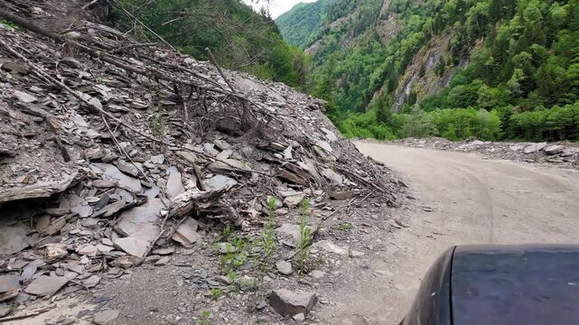 Point of view shot of a vehicle carefully maneuvering around a dangerous rockfall that has blocked a narrow mountain pass, highlighting the hazards of driving in remote, rugged terrain