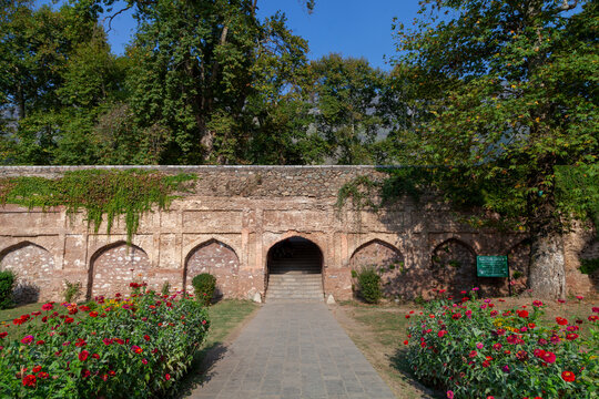 Two people sitting on stairs under an arch in an old stone garden wall with flower beds, Jammu and Kashmir, Srinagar, India