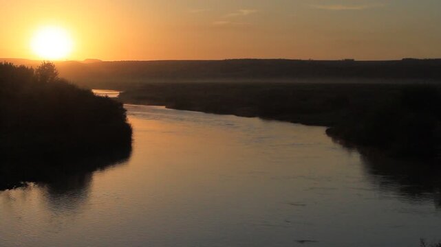 RAW and unedited stock footage capturing a beautiful golden sunrise over the historic Tigris River (Dicle River), with light morning mist rising from the water surface. Authentic, unprocessed landscap