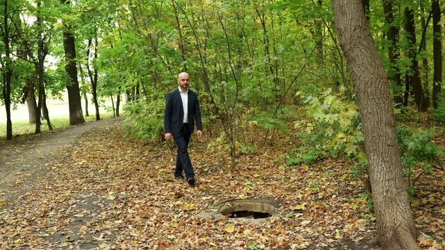 Unaware businessman stumbling into open manhole trap