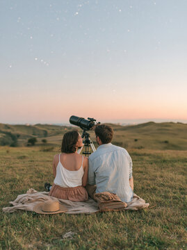 Young Couple Sitting on Blanket Watching Stars with Telescope at Sunset