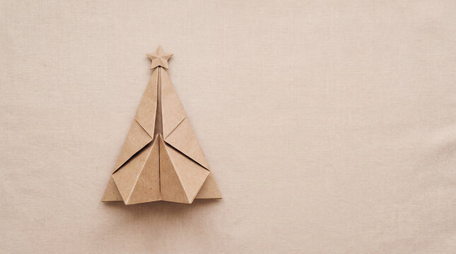 Minimalist origami Christmas tree made of brown paper with a star topper on a textured beige background