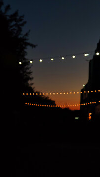 Outdoor blurred String Lights Hanging Against Beautiful Dark Evening Sunset Sky