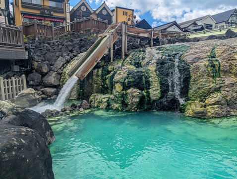 温泉街を背にした草津温泉の湯滝とエメラルド色の湯だまり 群馬県草津町