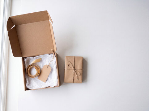 Sustainable kraft paper gift box with gold ribbon and blank tag, rustic e-commerce packaging set, minimalist parcel delivery for small business.